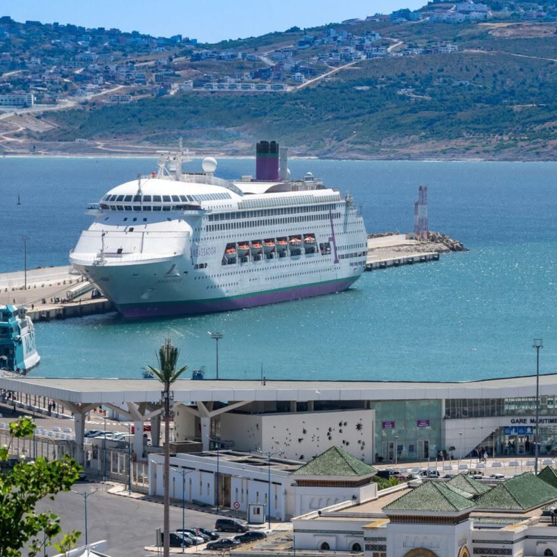 An Ambassador cruise ship docked at the Tangier maritime port in Morocco with rolling hills in the background.