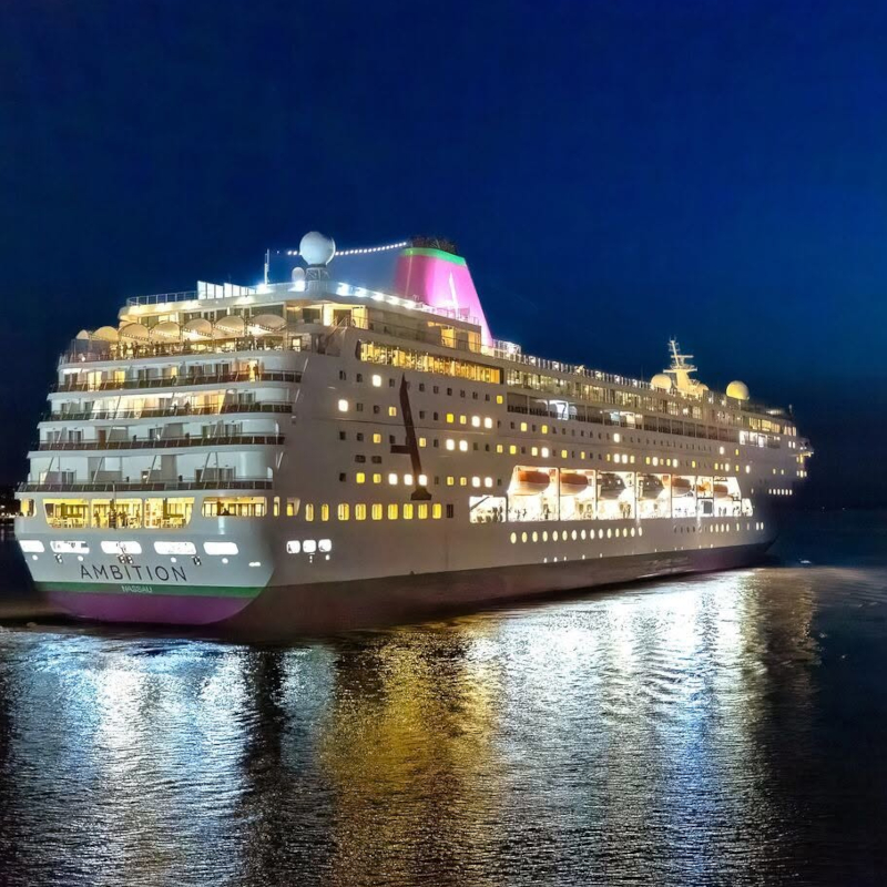 The illuminated cruise ship 'Ambition' sailing at night with its glowing lights reflecting on the dark water.