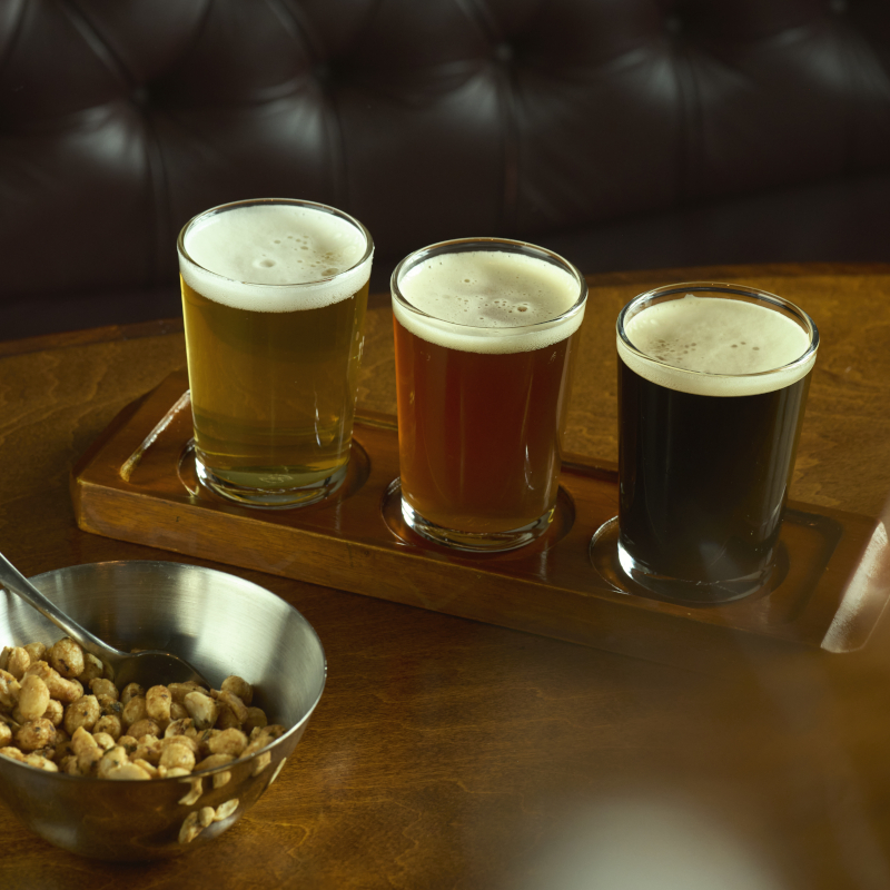 Three varieties of beer on a table next to a bowl of nuts