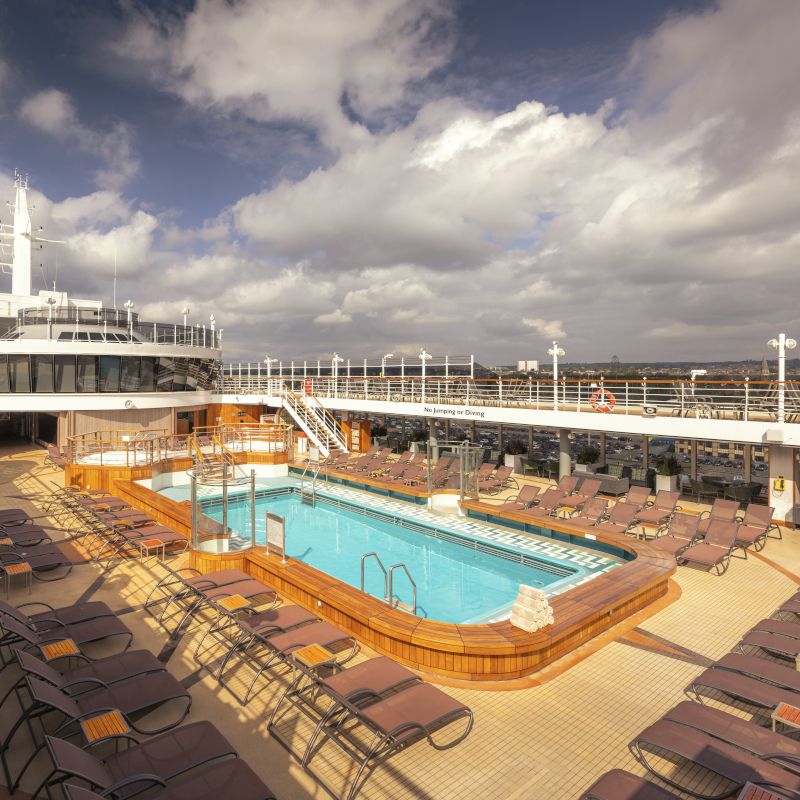 Open-air swimming pool on a cruise deck surrounded by lounge chairs.