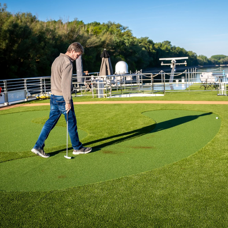 A man playing golf on a synthetic putting green located on the open sun deck of a river cruise ship.