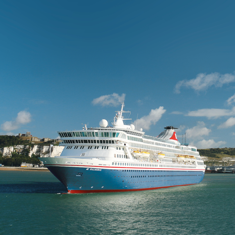 The Fred. Olsen cruise ship Balmoral sailing in calm waters near the White Cliffs of Dover under a bright blue sky.