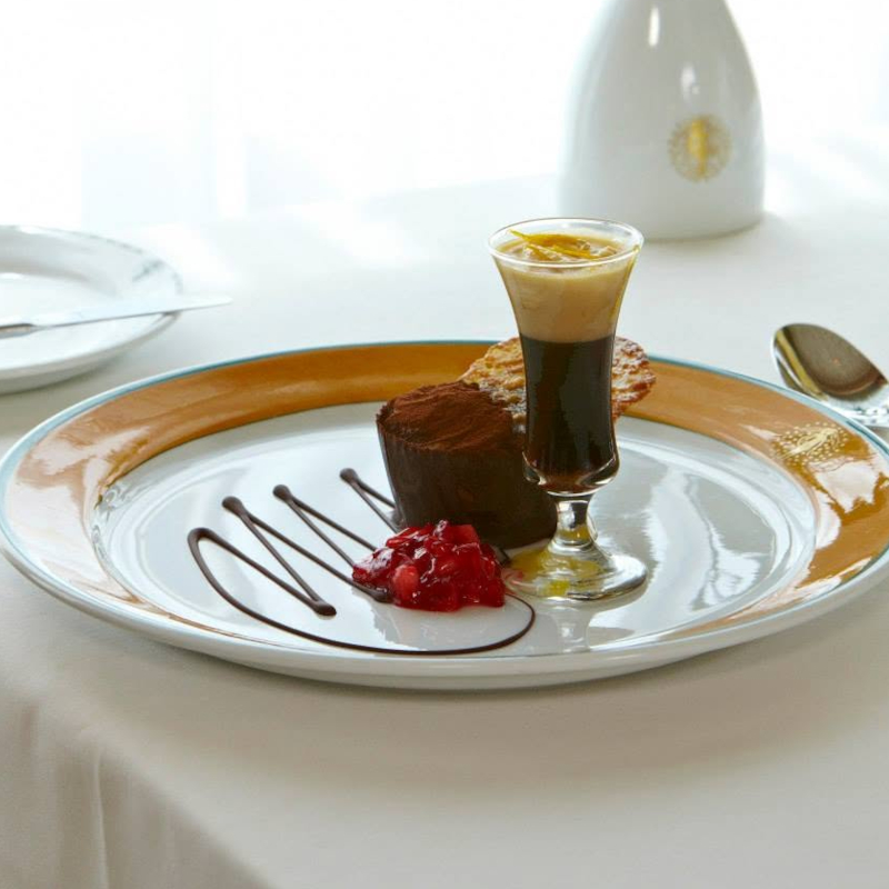 A plated chocolate dessert alongside a miniature layered espresso shot and red berry compote on a white tablecloth.