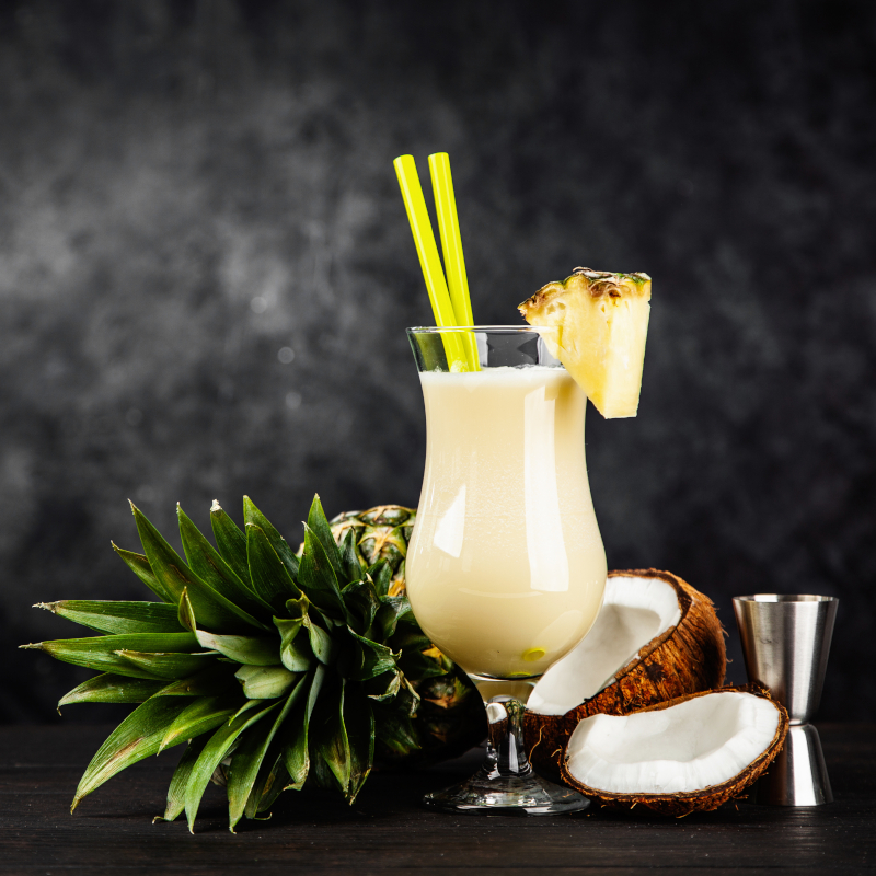 Creamy tropical Piña Colada cocktail garnished with a pineapple wedge alongside fresh coconut halves.