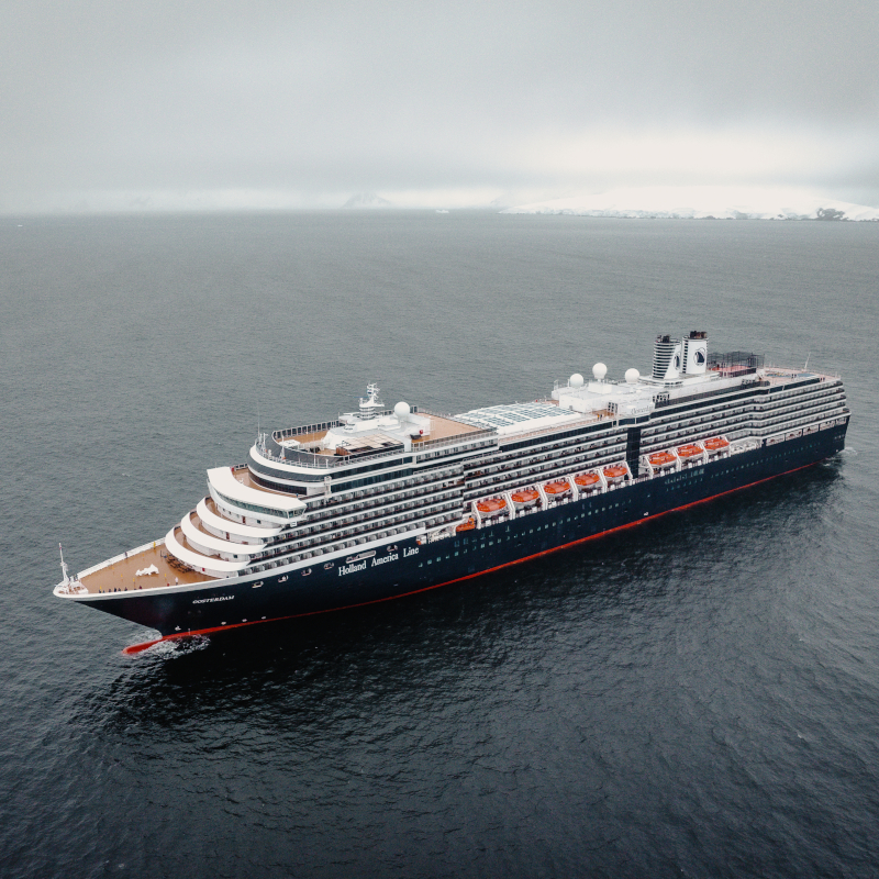 Aerial wide-angle view of a Holland America Line cruise ship navigating calm, deep grey water.