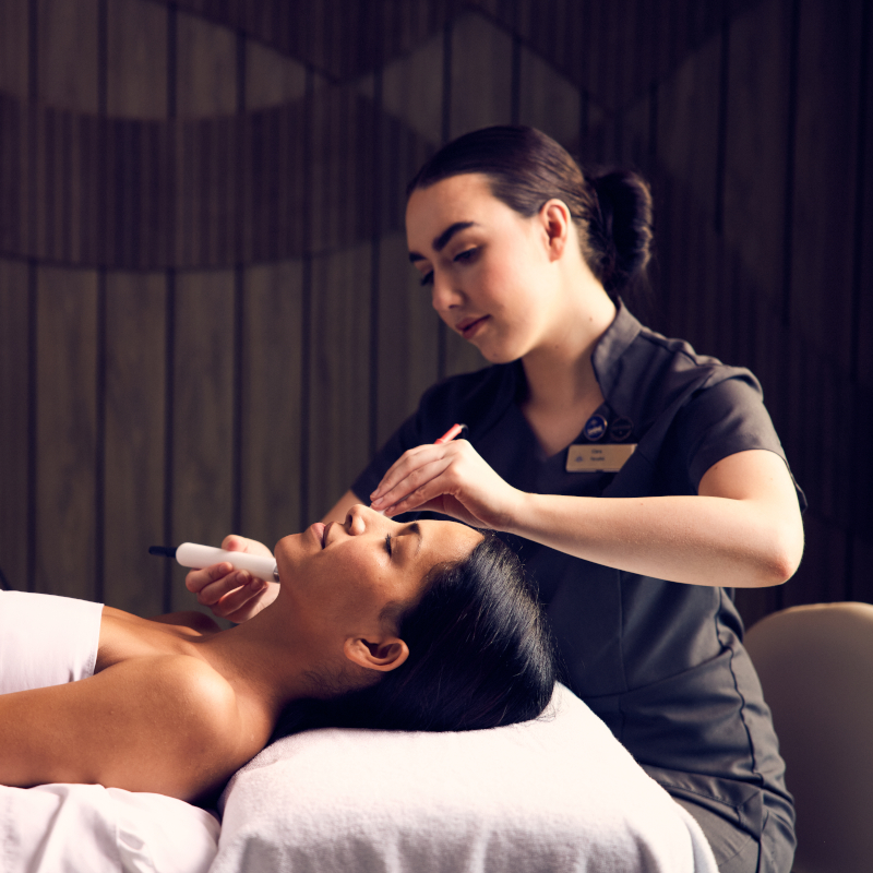 A woman receiving a relaxing facial treatment from a spa therapist on board.