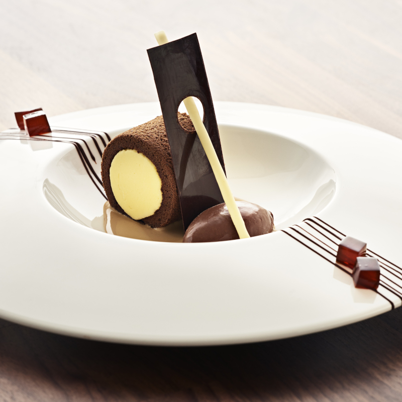 Gourmet rolled tiramisu dessert garnished with chocolate shards and a scoop of ice cream.