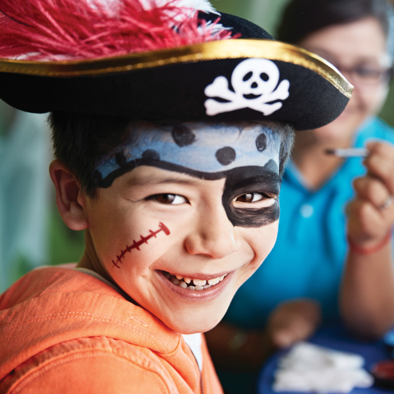 Young boy smiling with pirate-themed face paint and a costume hat.